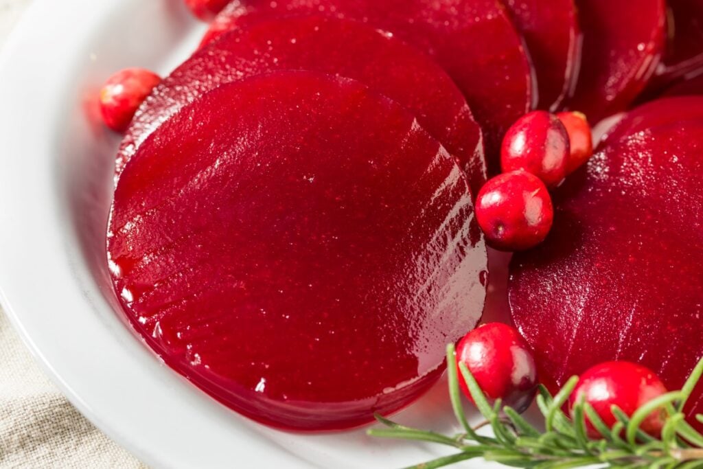 Slices of canned cranberry sauce arranged on a white plate, garnished with fresh cranberries and rosemary sprigs, creating a festive presentation.