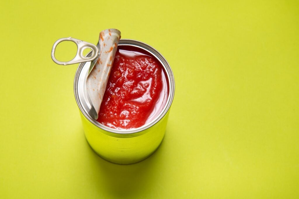 An opened can of tomato sauce sits on a bright yellow background.