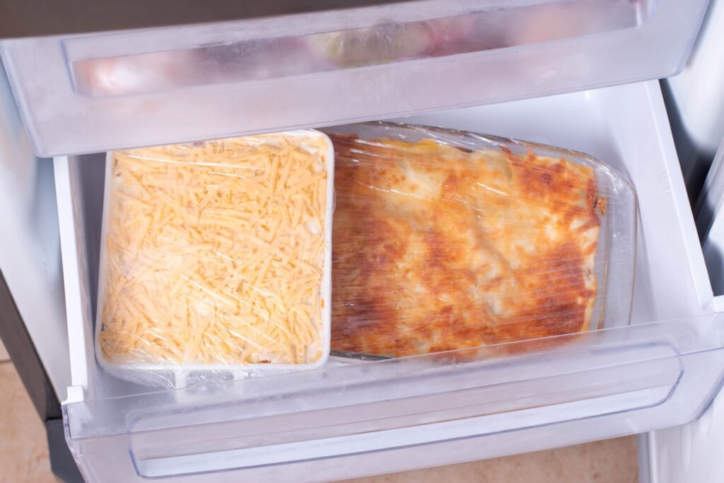 Two casseroles wrapped in plastic wrap stored in a freezer.