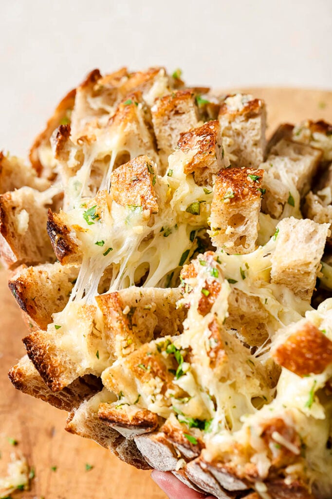 Close-up of a cheesy garlic pull apart bread loaf, showing melted cheese and herbs nestled in between.