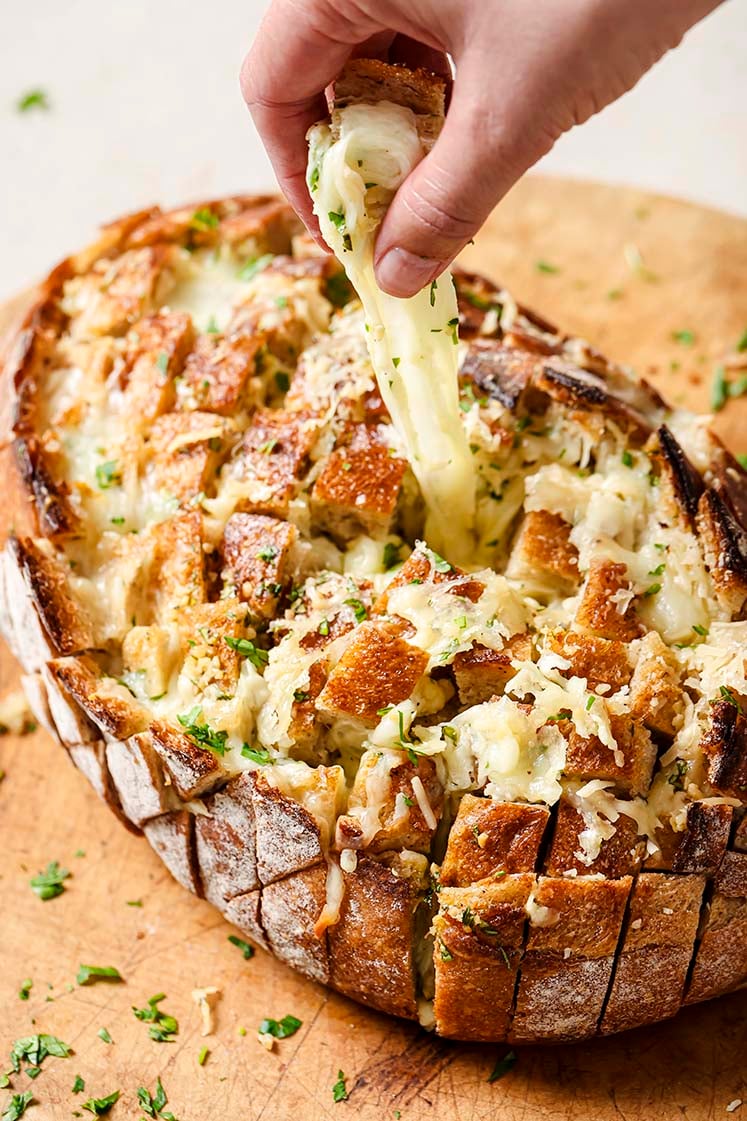 A hand pulls a piece of from the cheesy garlic pull apart bread, revealing melted cheese.