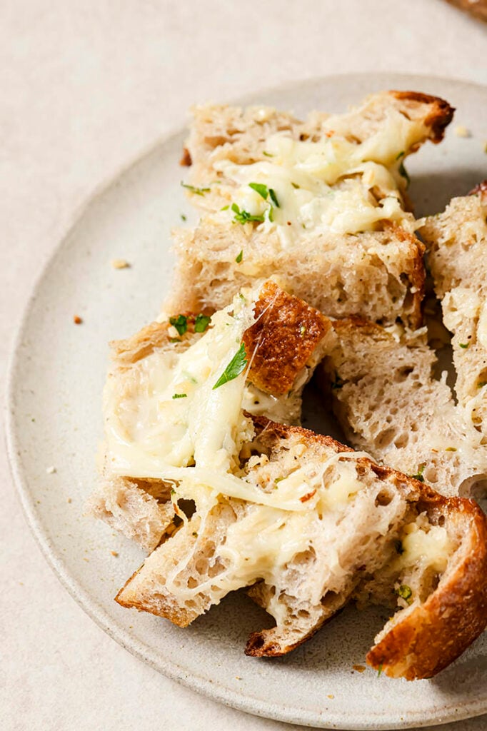 Cheesy garlic pull apart bread cubes, showing melted cheese and herbs on a plate.