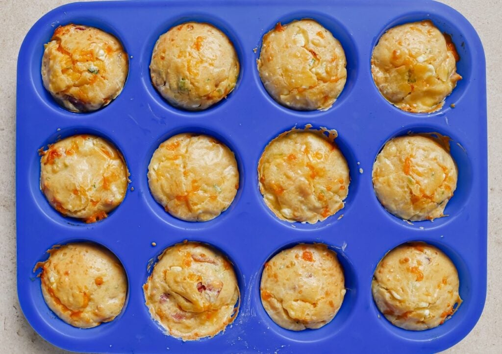 A blue silicone muffin tray filled with freshly baked golden brown muffins, each in their own compartment. The muffins appear soft and slightly crispy on top.