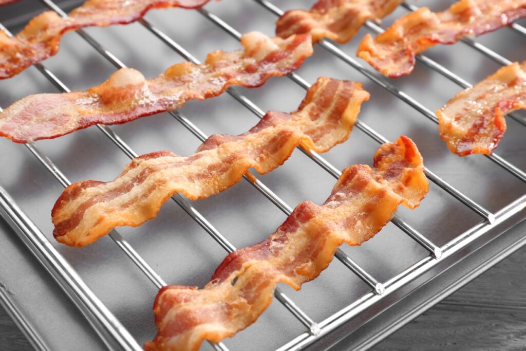 Strips of crispy, cooked bacon are laid out on a wire rack over a baking sheet. The bacon appears golden brown with a slightly wavy texture.