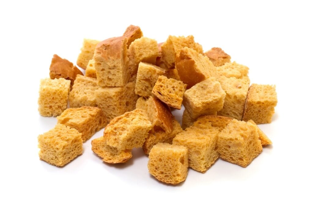 A pile of golden brown croutons isolated on a white background. The croutons are cubed, showing a light and airy texture.