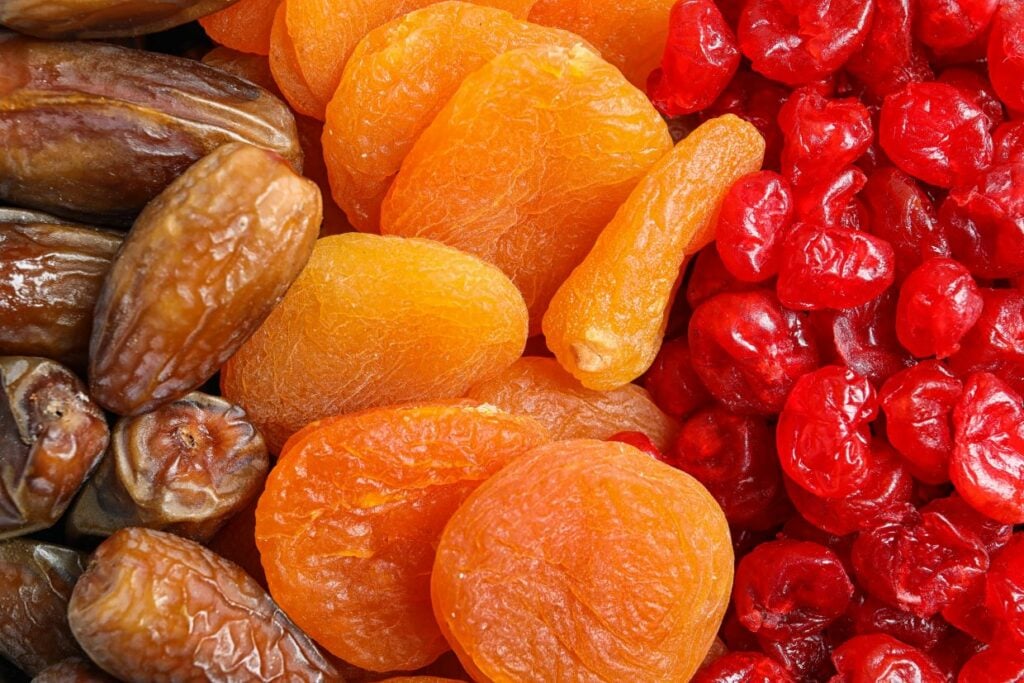 Close-up of assorted dried fruits including brown dates, orange apricots, and red cherries arranged side by side, showcasing their vibrant colors and textures.