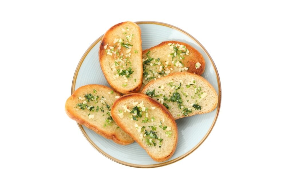 A plate with five slices of garlic bread topped with finely chopped parsley and garlic, displayed on a light blue dish against a white background.