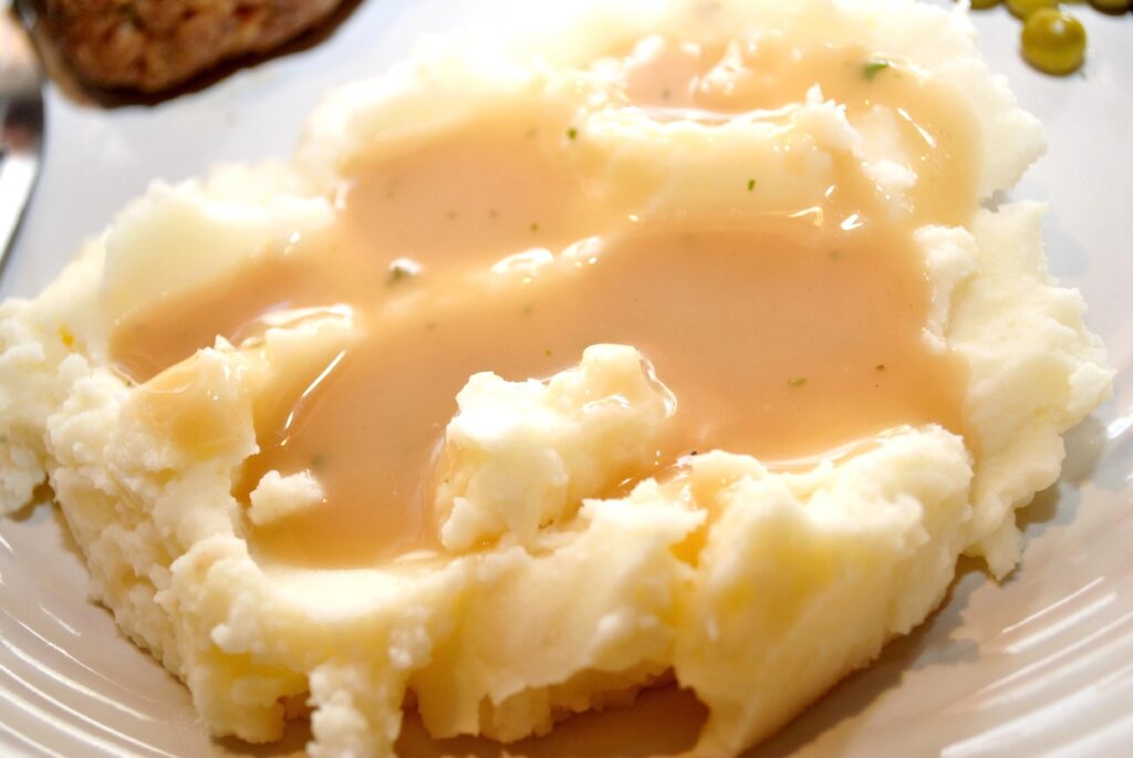 A serving of mashed potatoes topped with creamy gravy on a white plate.