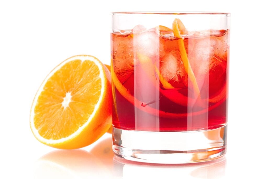 A glass of negroni near a halved orange.