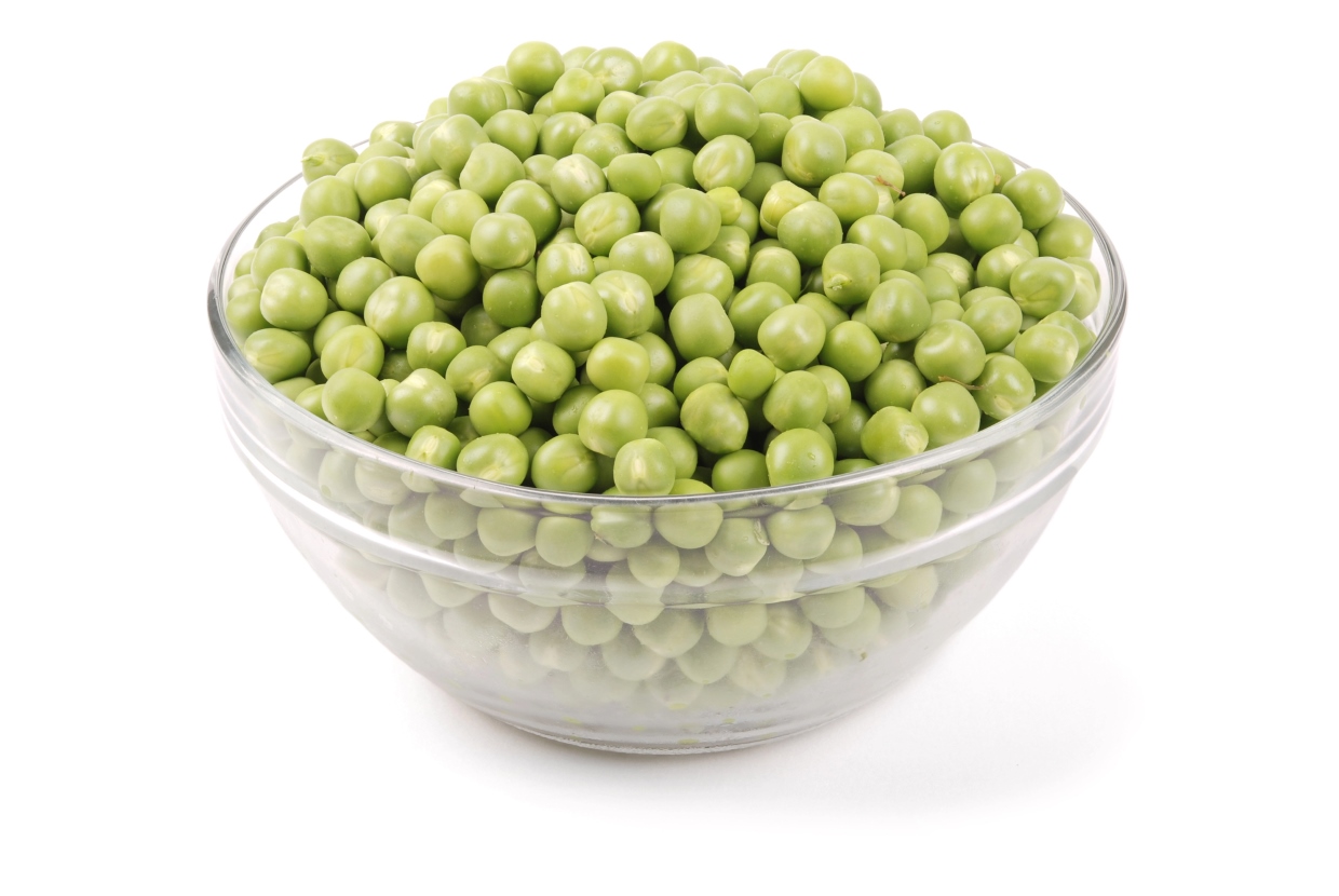 A clear glass bowl filled with fresh green peas, placed on a white background.