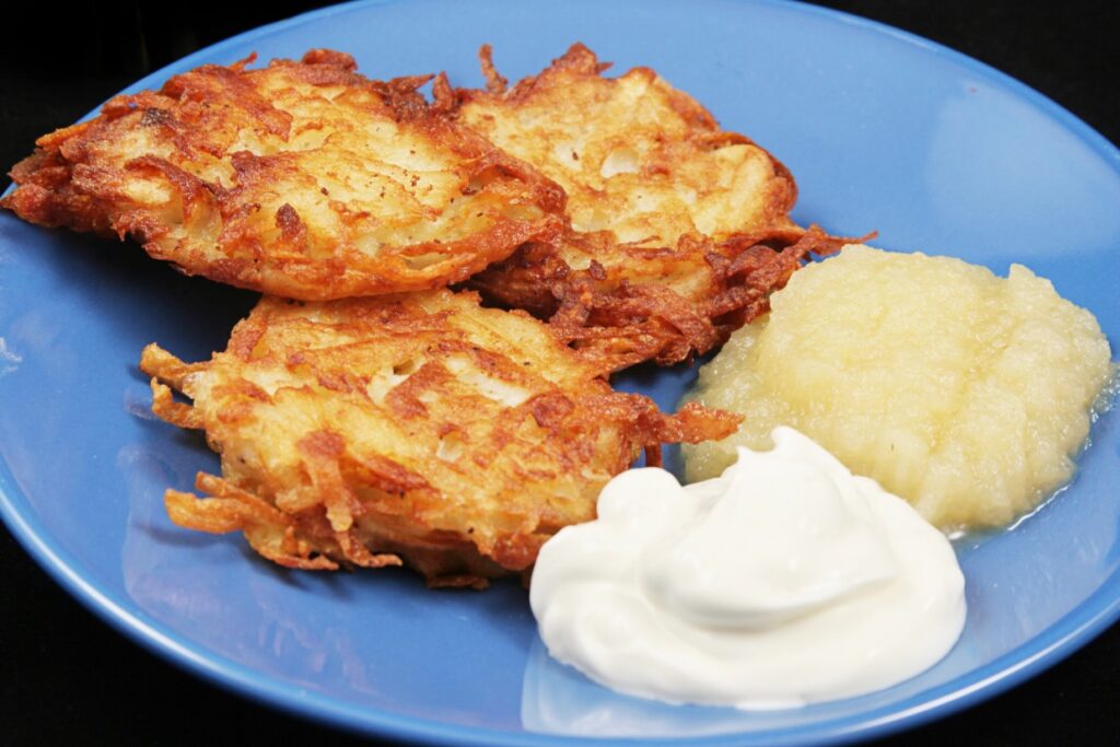 Potato latkes on a blue plate with applesauce and sour cream.