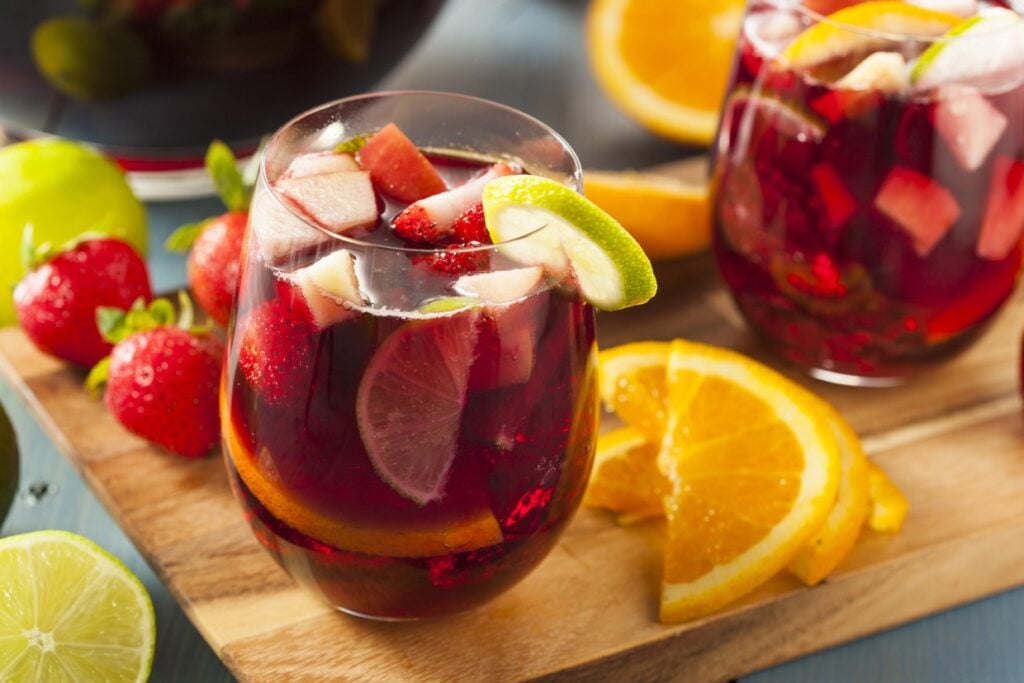 Sangria glasses garnished with lime slices next to orange slices and whole strawberries.