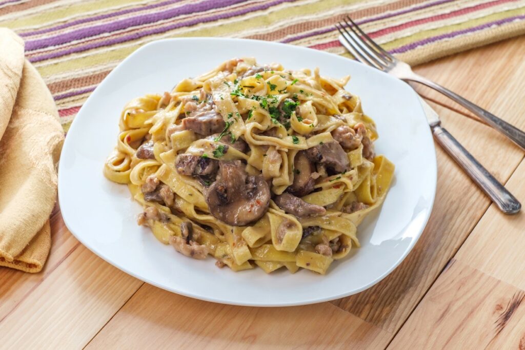 A plate of creamy mushroom fettuccine garnished with parsley, served on a wooden table with a striped napkin. A fork rests beside the plate.