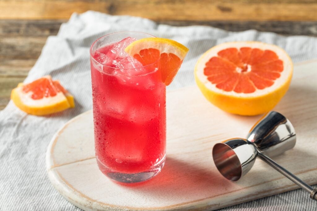 Sea breeze cocktail garnished with grapefruit wedge near a halved grapefruit.