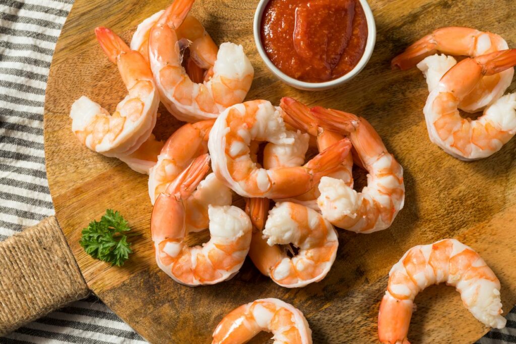 Cooked shrimp with cocktail sauce on a wooden serving tray.