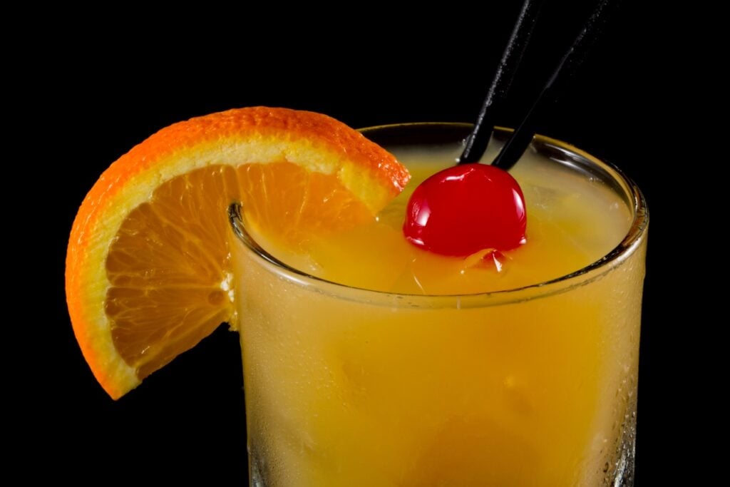 Whiskey sour cocktail with a cherry, orange slice, and two straws.