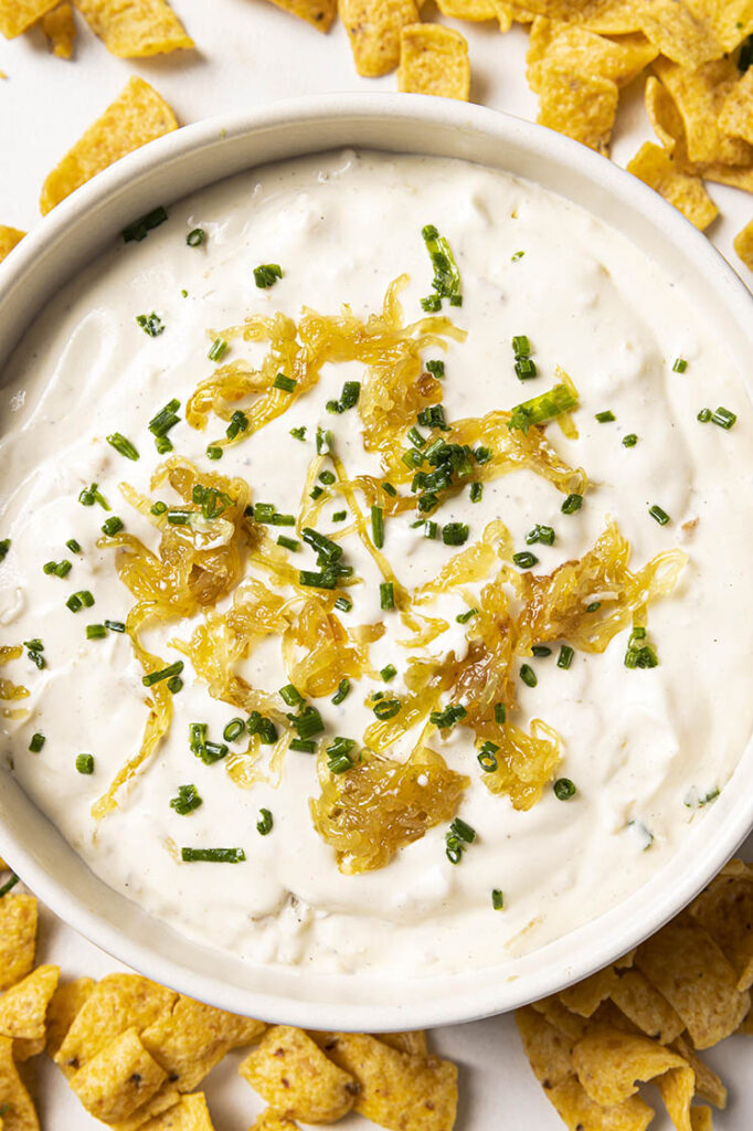 A bowl of caramelized onion dip garnished with caramelized onions and chopped chives, surrounded by crispy corn chips.