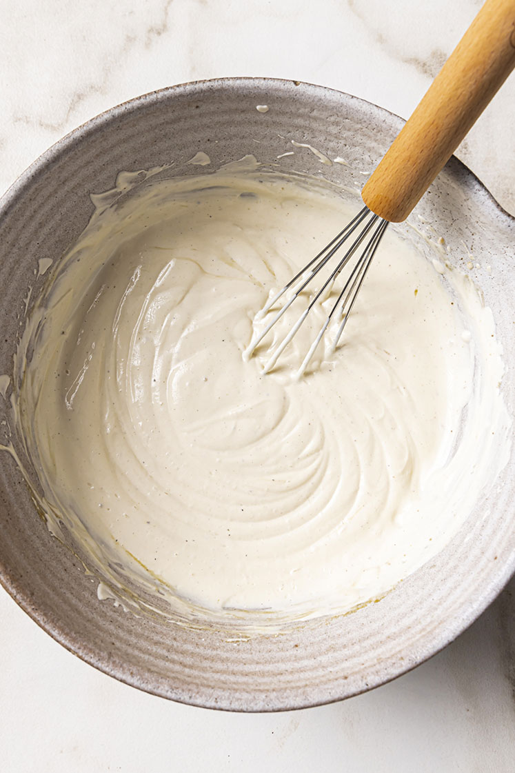 A ceramic bowl filled with creamy white mixture with a whisk.