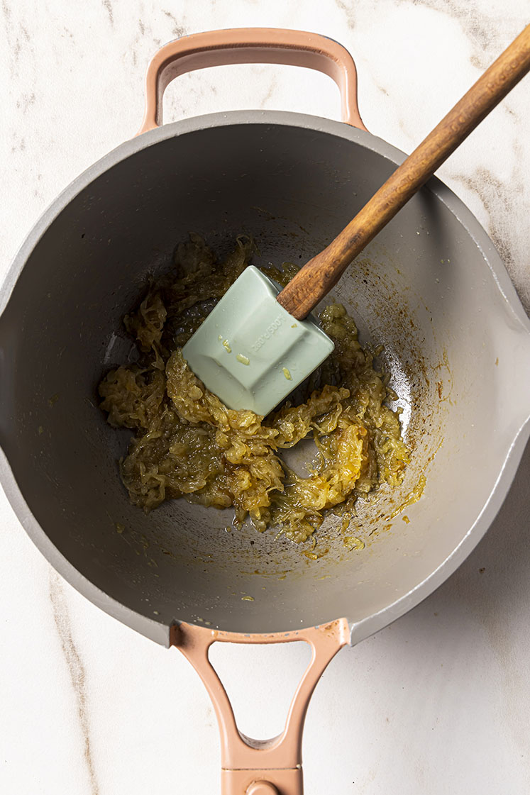 A pot with caramelized onions being sauteed by a spatula with a wooden handle.