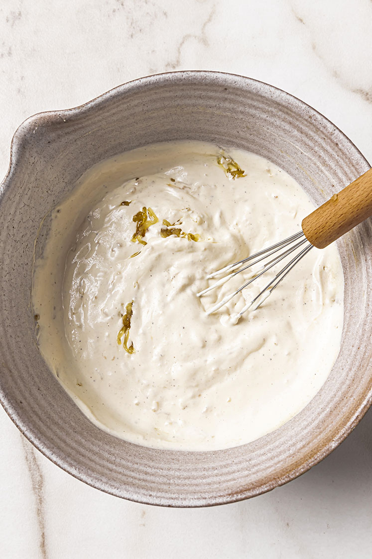 A ceramic bowl with the creamy white dip and caramelized onions, being mixed by a whisk.