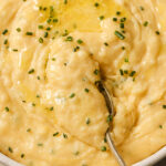 A bowl of cheddar and chive mashed potatoes with a spoon.