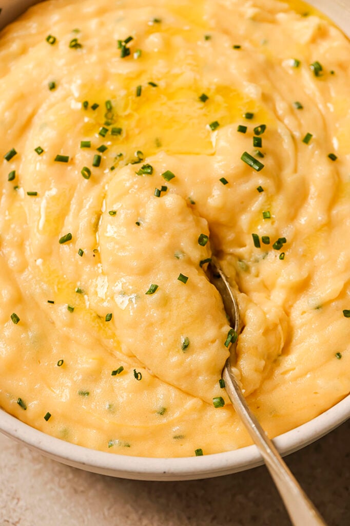 A bowl of cheddar and chive mashed potatoes with a spoon.