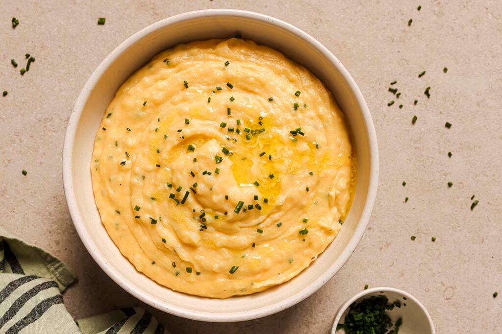 A bowl of garnished cheddar and chive mashed potatoes.