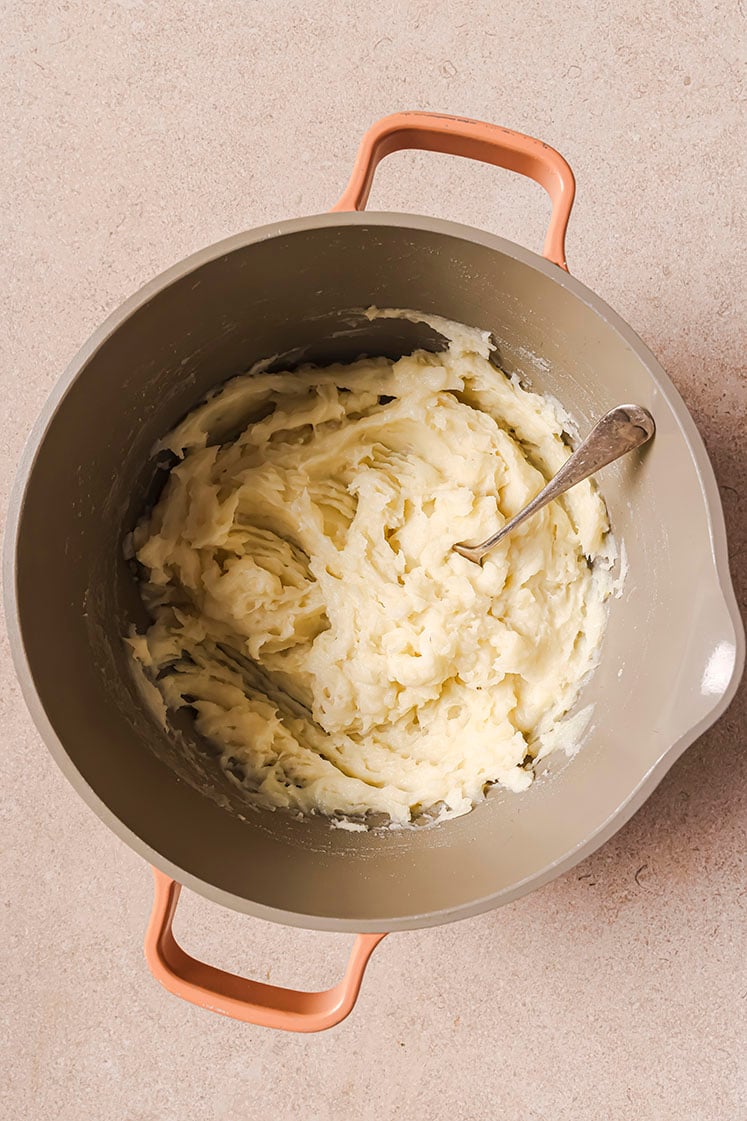 A pot of creamy mashed potatoes with a spoon.