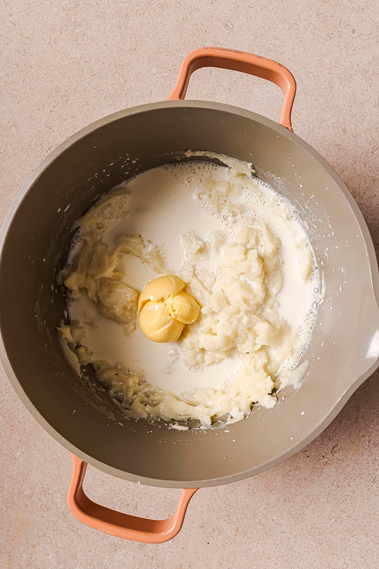 A pot with mashed potatoes, milk, and a dollop of butter.