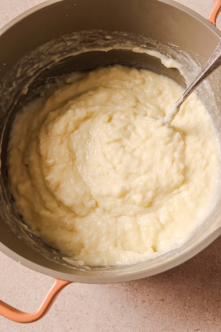 A pot with creamy mashed potatoes, being stirred with a spoon.