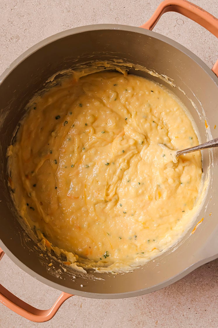 A pot with cheddar and chive mashed potatoes with a spoon.