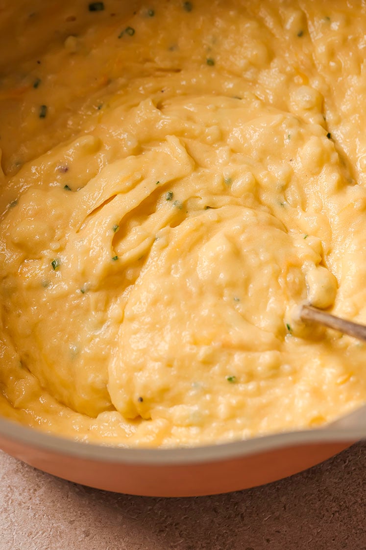 A pot with cheddar and chive mashed potatoes with a spoon.