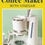 A white coffee maker with an empty glass carafe is displayed on a counter. A jar of coffee grounds is nearby. Text on the image reads, "Cleaning a Coffee Maker with Vinegar." The background is a light green wall.