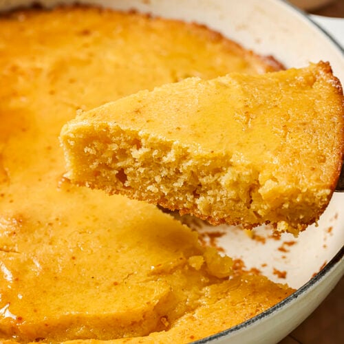 A slice of honey butter skillet cornbread being lifted from a round dish.