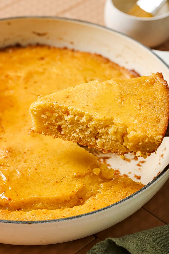 A slice of honey butter skillet cornbread being lifted from a round dish.