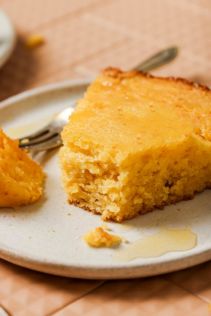 A slice of honey butter skillet cornbread with honey drizzle on a plate with a fork.