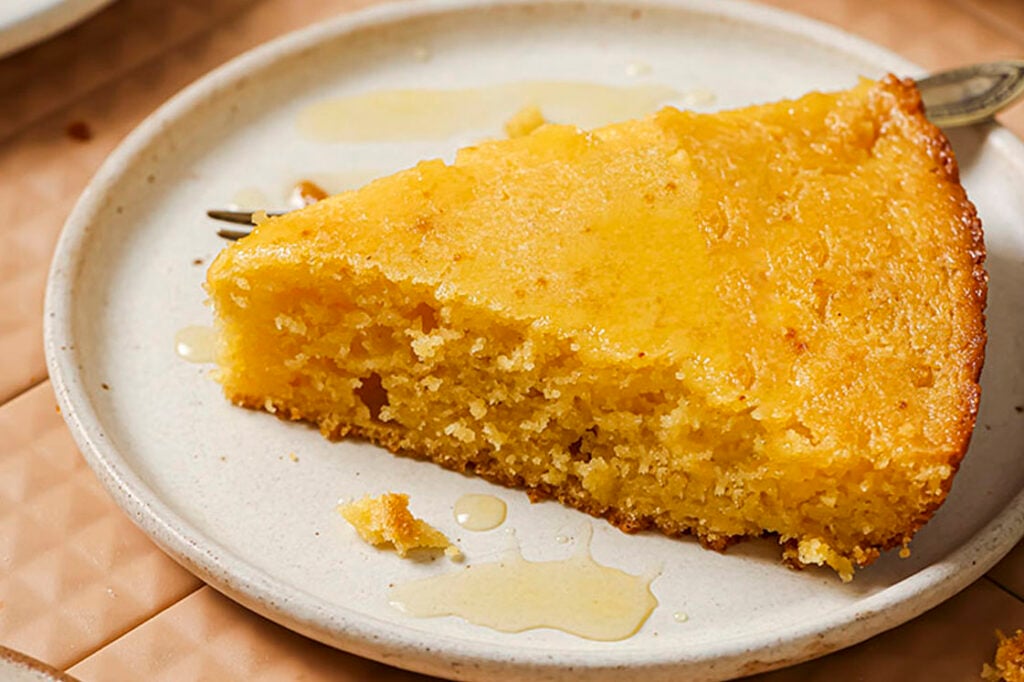 A slice of honey butter skillet cornbread with honey drizzle on a plate with a fork.