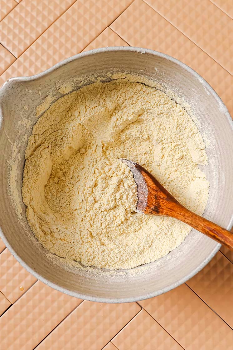 Dry ingredients in a mixing bowl with a wooden spoon.