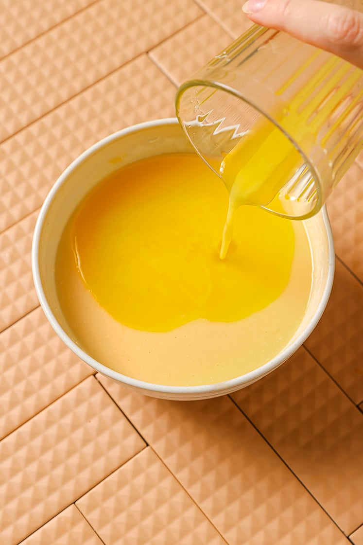 A person pours melted butter into a mixing bowl with the wet ingredients.