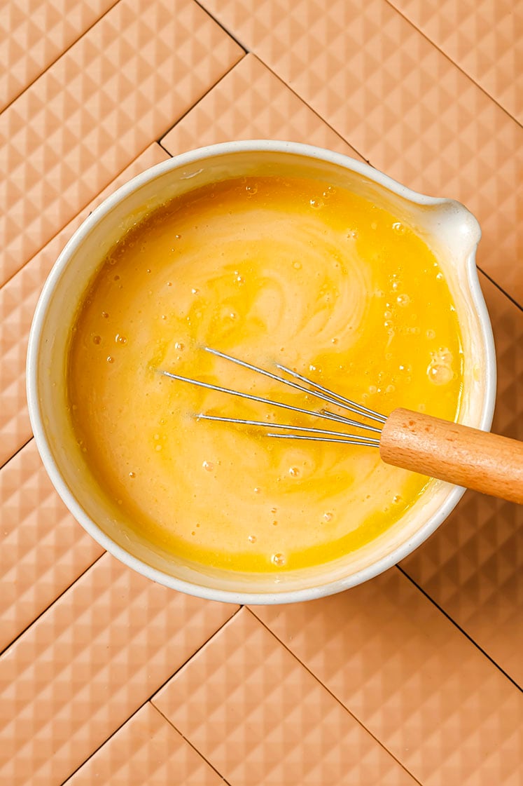 Wet ingredients in a mixing bowl being mixed by a whisk.