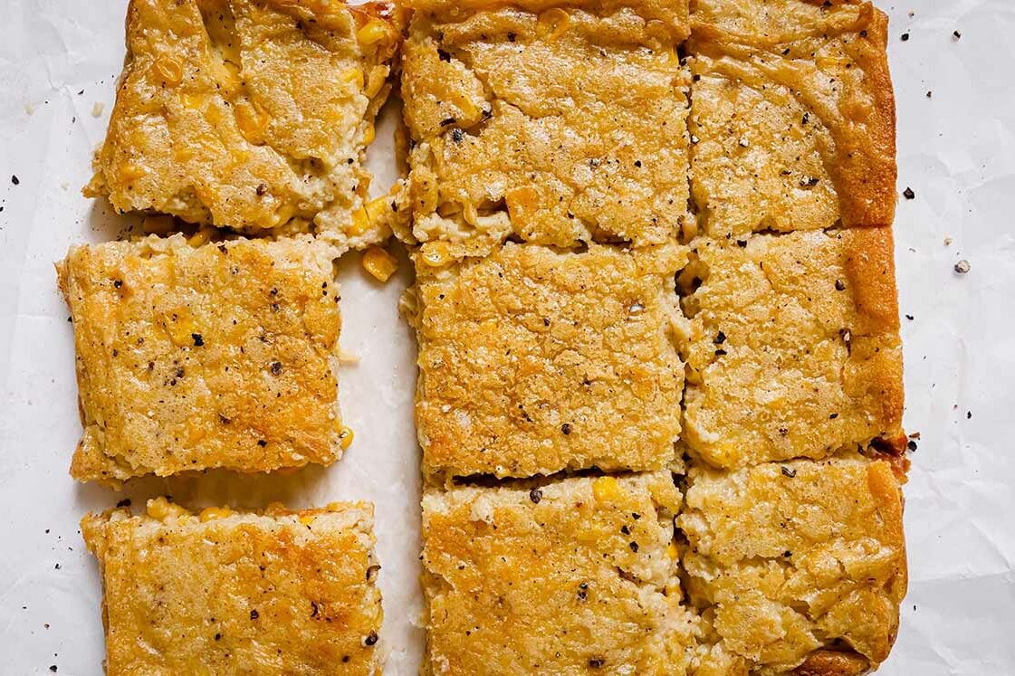 Sliced Jiffy corn casserole on parchment paper, seasoned with black pepper.