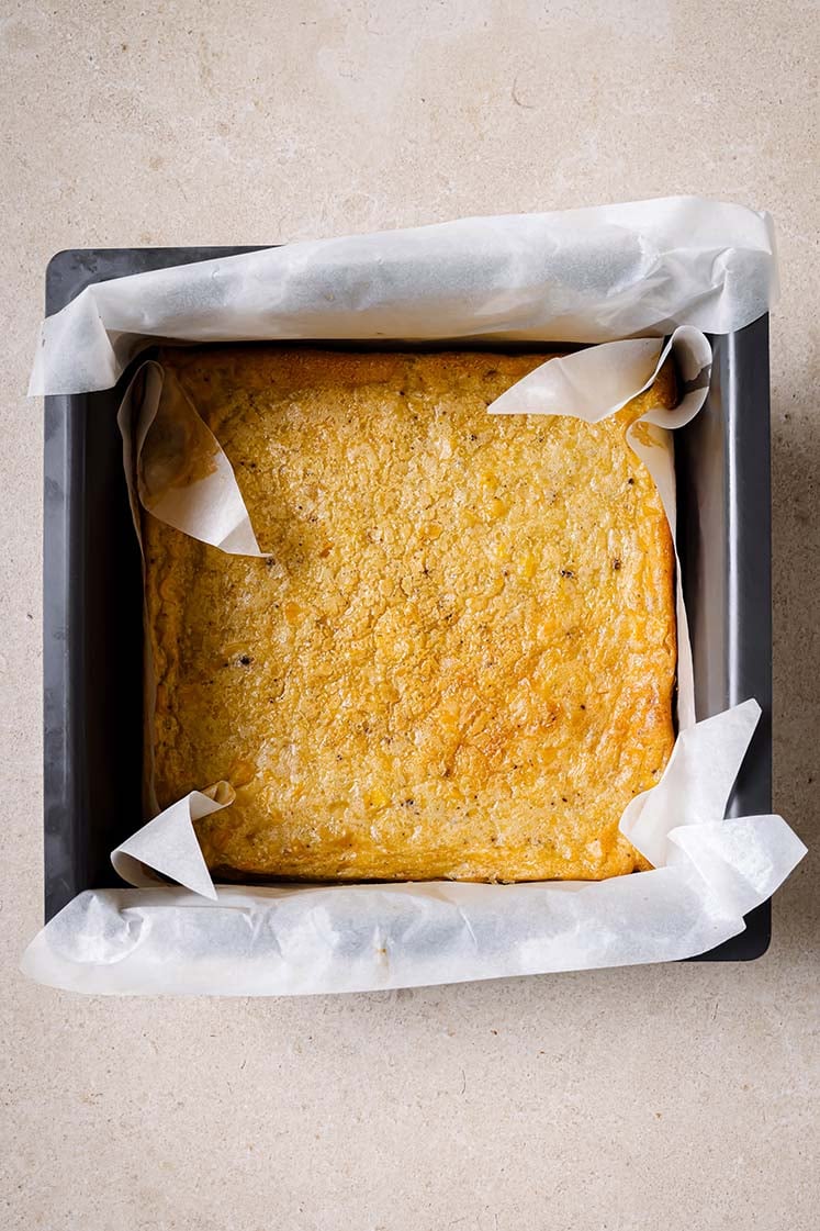 A square baking pan lined with parchment paper, with baked Jiffy corn casserole.