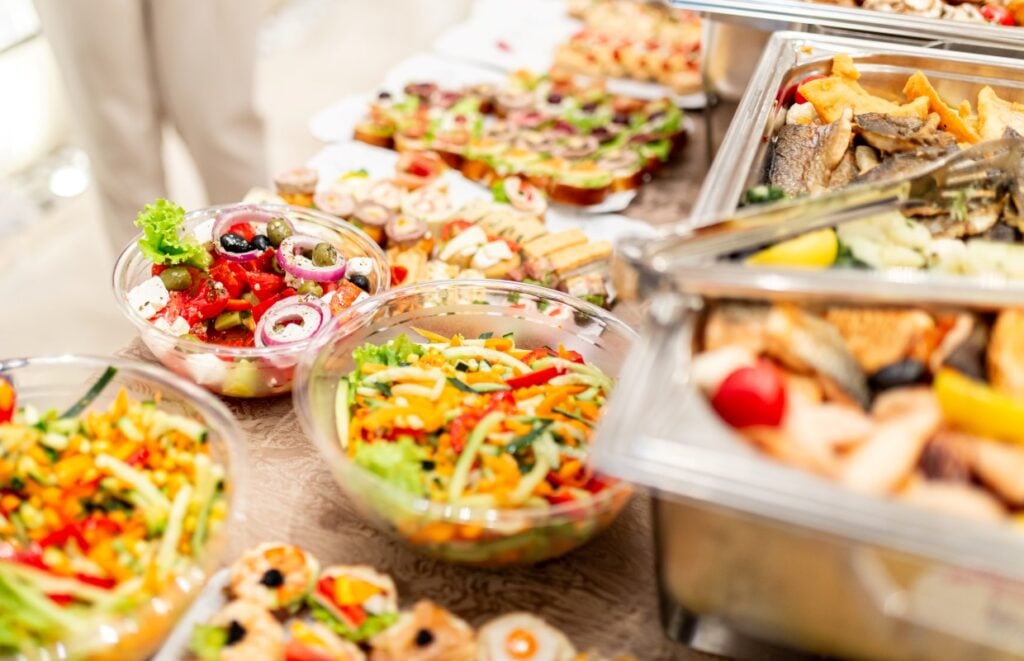 A buffet table filled with a variety of colorful dishes, including bowls of mixed salads, trays of assorted appetizers, and platters of grilled fish and vegetables.