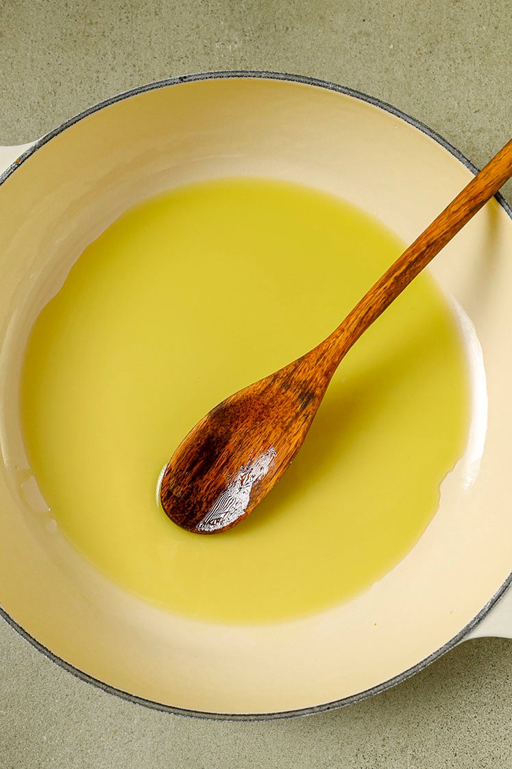 Olive oil in a skillet with a wooden spoon.