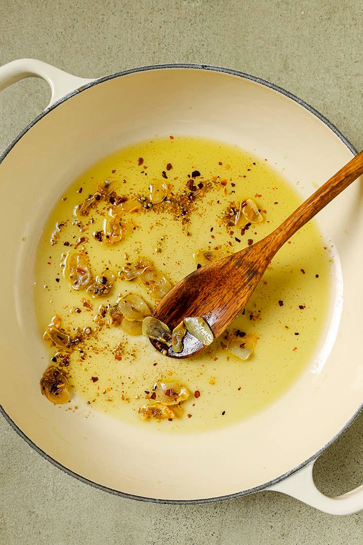 Olive oil, garlic, and spices in a skillet with a wooden spoon.