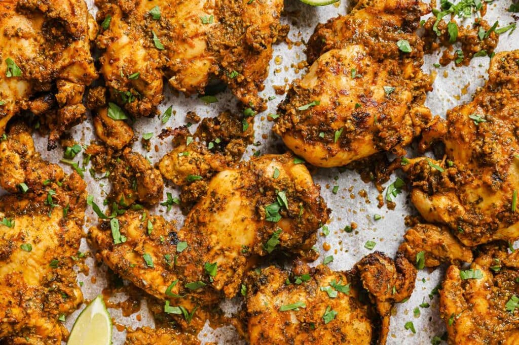 Garnished pollo asado with lime wedges on a baking sheet.