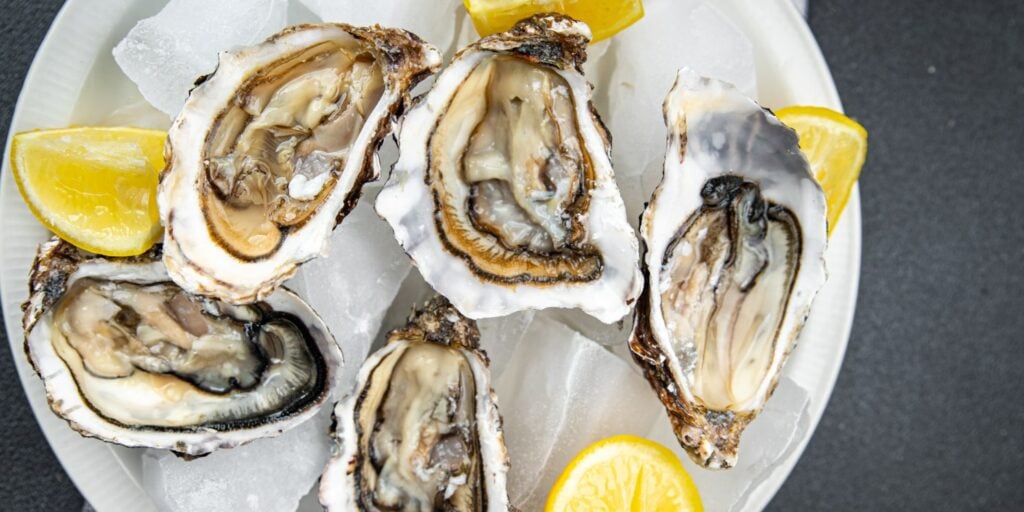 A plate of fresh oysters served on ice with lemon wedges, showcasing opened oyster shells and their moist, briny insides.