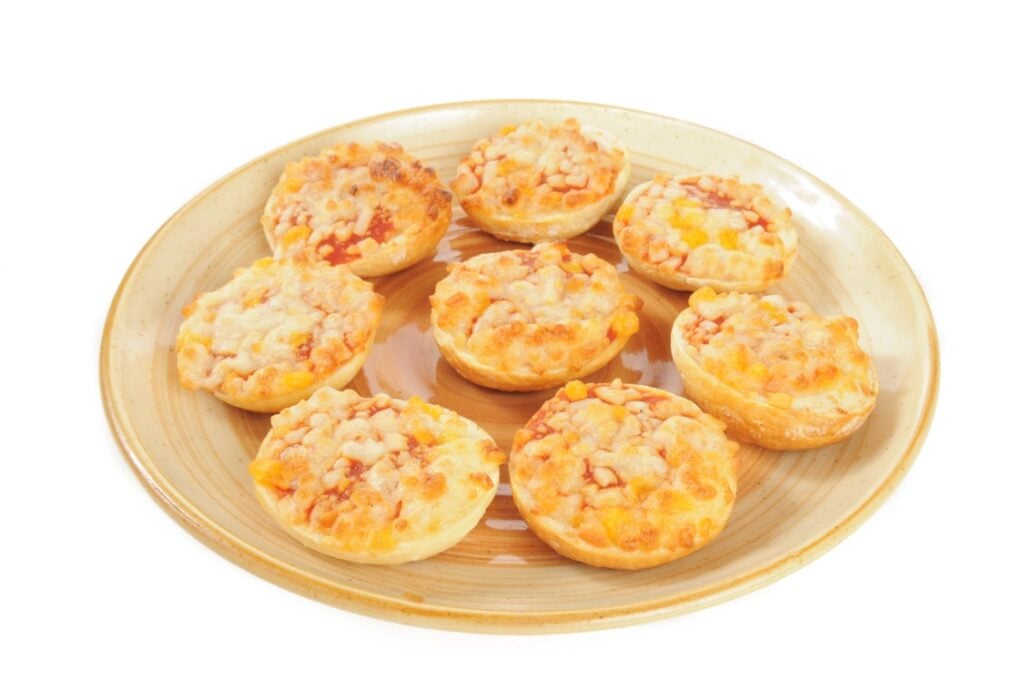 A beige plate with eight small, round, baked mini pizzas topped with melted cheese and bits of tomato sauce, set against a white background.
