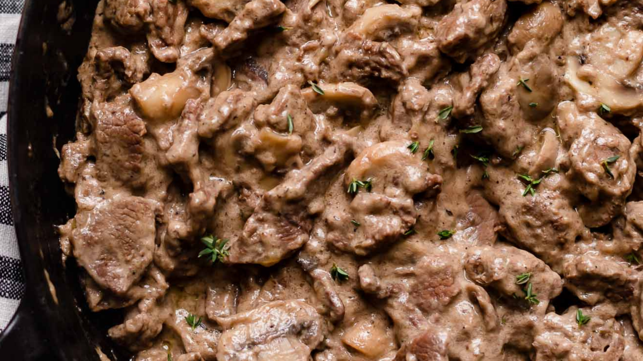 A black skillet filled with creamy beef stroganoff and sautéed mushrooms, topped with garnish.