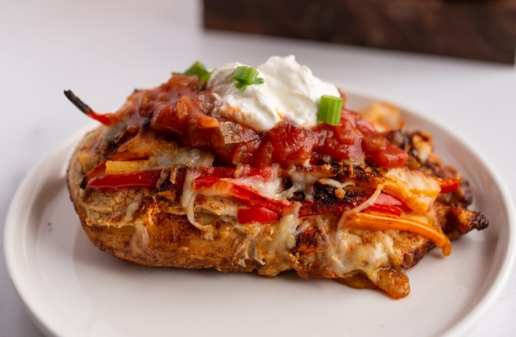 A stuffed chicken breast topped with salsa, shredded cheese, sour cream, and chopped green onions on a white plate. Strips of red and yellow bell peppers are visible inside the chicken.